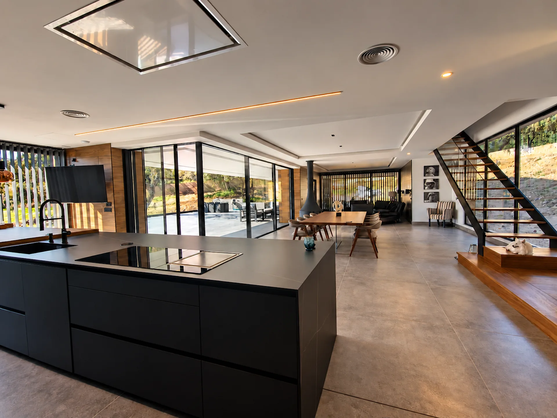 Cocina y salón de una reforma integral de Loretta Interiorismo: isla negra, grandes ventanales y escalera de madera